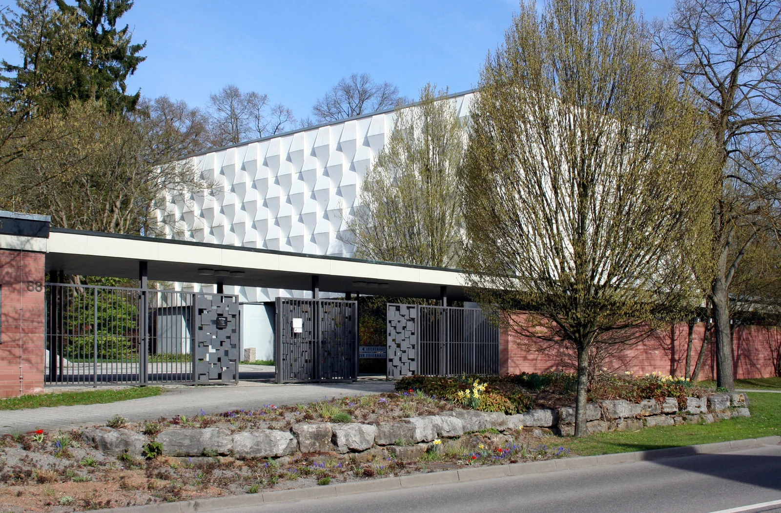 Eingangsbereich mit moderner Feierhalle und markanter weißer Dachfassade auf Friedhof Feuerbach